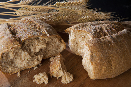 Organic wholemeal bread on a wooden table with wheat ears of corn