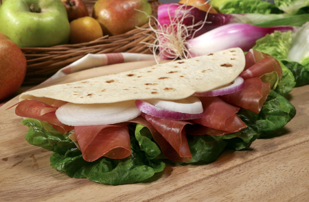 Piadina Italiana with ham, salad, onion, on a wooden cutting boardの写真素材
