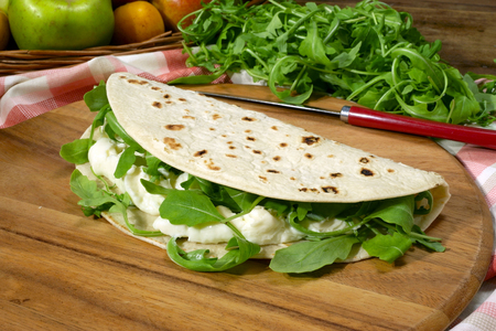 Piadina Romagnola stuffed with stracchino and rocket on a wooden cutting boardの写真素材
