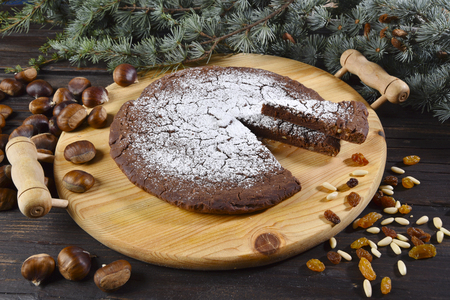 Castagnaccio, typical Italian sweet bread with sultanas and pine nuts, on a wooden cutting boardの写真素材