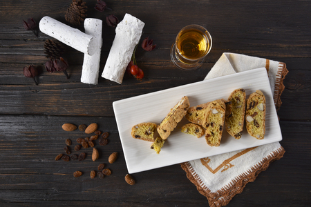 Cantucci with almonds and sultana grapes on a wooden table served with a glass of holy wineの写真素材