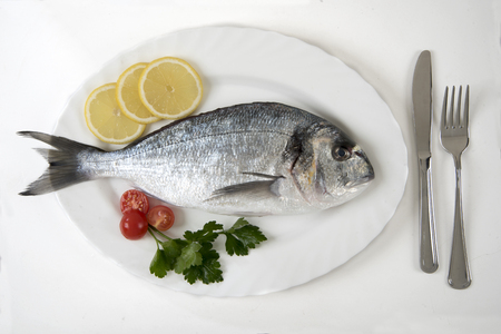 Fresh sea bream fish on an oval dish with parsley and cherry tomatoesの写真素材