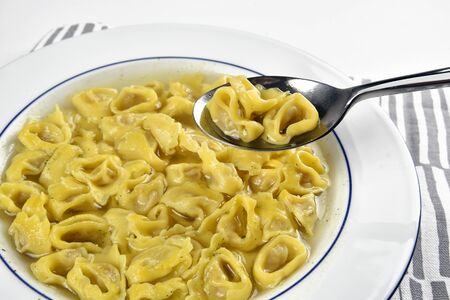Dish with tortellini in broth and a spoon with some tortelliniの写真素材