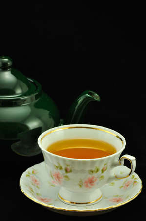 porcelain tea cup full of tea and green teapot on a black backgroundの写真素材