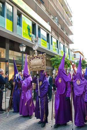 Penitents in purple hoods (capirotes) and wearing long purple tunic walk ahead of float with Jesus...