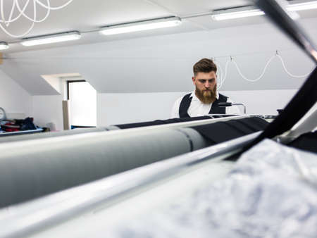 Young bearded tailor working on new clothing design