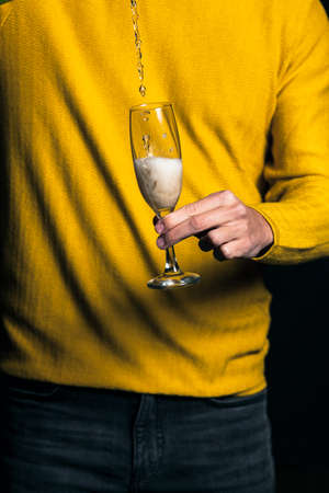 Young man in yellow sweater pour champagne in a glassの写真素材