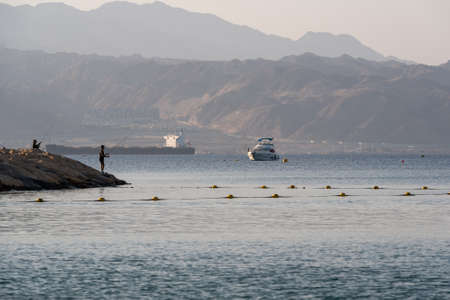 Men fishing on the pier in the early morning in Eilat, Israel with the view of Jordan in the...