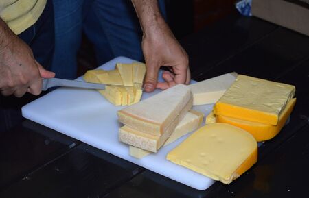 Man cutting different cheese types with knife on white cuttingboard.の写真素材