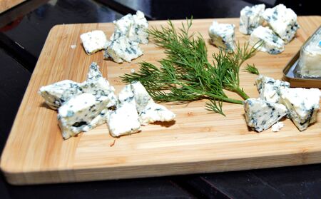 Fresh made platter with danish blu cheese pieces and green dill on wooden boardの写真素材