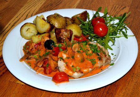 Dish with fried meat, vegetables, baked potatoes and fresh herbs and cherry tomatoの写真素材
