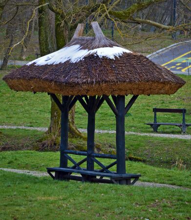 Wooden gazebo covering bench in park, covered by melting snow in springの写真素材