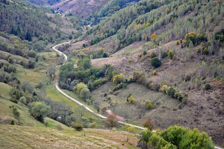 Old rural road along valley, surrounded by hills covered in vegetation and treesの写真素材