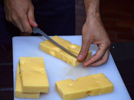 Man holding cheese knife, cutting Swiss cheeses on a white cutting board, preparing a traditional cheese platterの写真素材