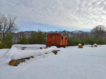 Winter landscape somewhere in the Carpathian Mountains, in a clearing of an evergreen forest there is an old, rusty, abandoned train cart surrounded by pristine snow.の写真素材