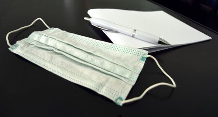 Paper notepad for notes next to pen and a surgical/medical face mask, taking notes during the world pandemicの写真素材