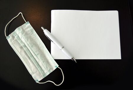 Closeup shot of notepad, pen and mask,, facemask on desk next to paper notepad and pen great for headlineの写真素材