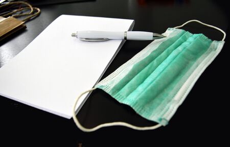 Containment surgical face mask next to paper notepad and pen on a deskの写真素材