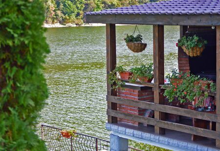 A small house by the lake, great destination for vacations, an outdoor garden by the waterfront, lakeview pattio with hanging plants, truly relaxing placeの写真素材