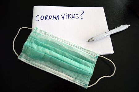 Coronavirus written on a notepad with a pen on a desk with facemask compositionの写真素材