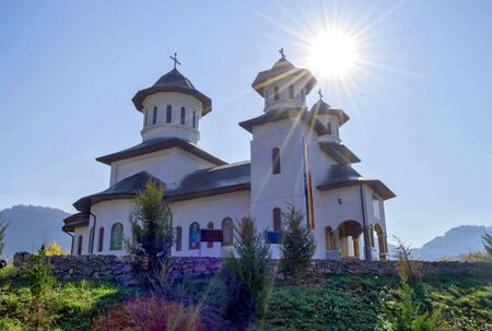 An orthodox chirstian church in Ponoarele, Romania, a spiritual place of worship, traditional romanian style white church in the middle of the mountains, with natural landscape and sunlight reflectingの写真素材