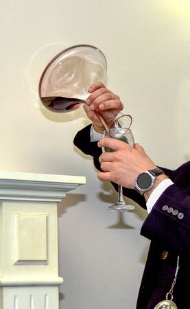 Close-up of expert sommelier or oenologist man dressed in formal black clothes pouring red wine from a decanter into a glass for a tastingの写真素材