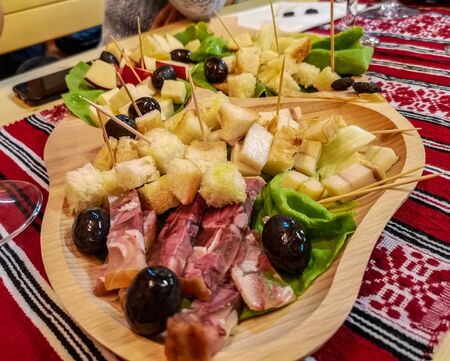 A rustic platter with cold cuts: ham, cheese, olives and other traditional finger foods, a common Romanian appetizer served on a wooden plateの写真素材