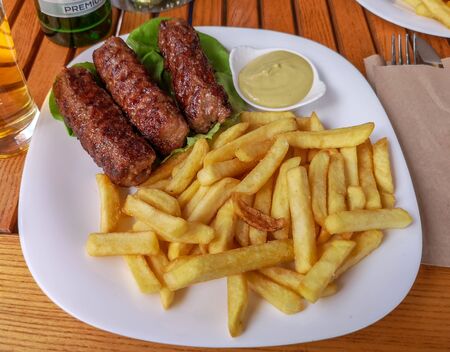 A classic, traditional romanian dish from mixed minced meats called "mici", served on a plate with fries and mustard, a go-to romanian meal during summerの写真素材