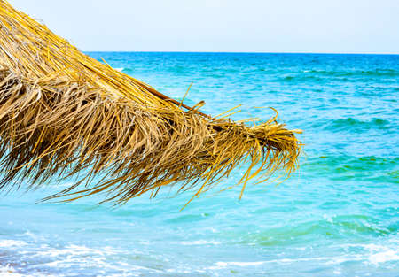 Close-up of straw beach umbrellas providing shade near the wavy water of the Black Sea on sandy shoreline on a sunny clear summer day at Vama Veche, Romaniaの写真素材