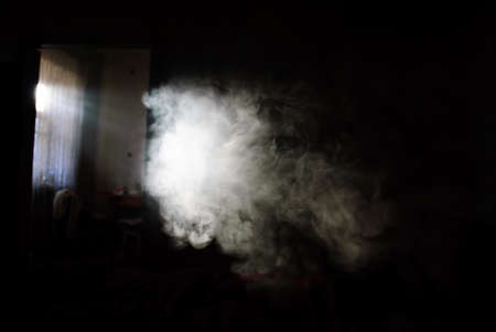 Fluffy Puffs of Smoke and Fog on Black Background and the sun's rays through the windowの写真素材