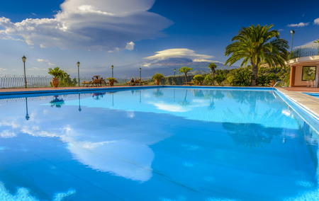 Etna mountain view from a swimming pool with some tourists enjoying their summer vacation