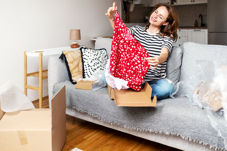 Happy woman unpacking parcel with her new summer dress online purchase from internet store.