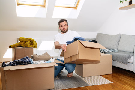 Volunteer man packing his old apparel into cardboard boxes at home, reusing, second hands concept.