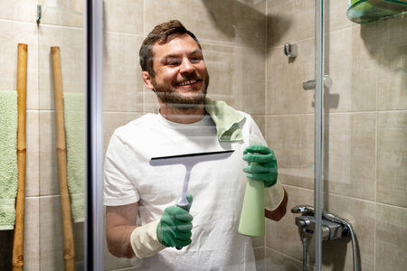 Smiling man cleaning glass wall in shower room.の写真素材