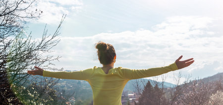 Woman with arms outstretched greeting nature while standing on hill in countryside.