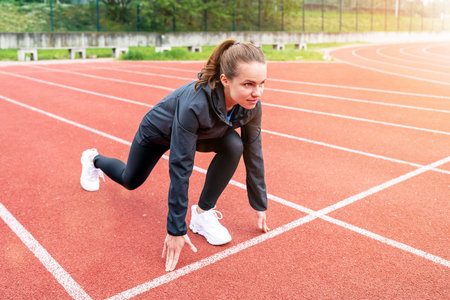 Brunette woman runner in start position on running track while workout.
