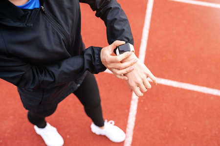 Athlete female person standing on running tracks and using her digital wrist watch.