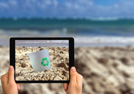 Recyclable materials concept, digital tablet in hands scanning beach sand for litter.