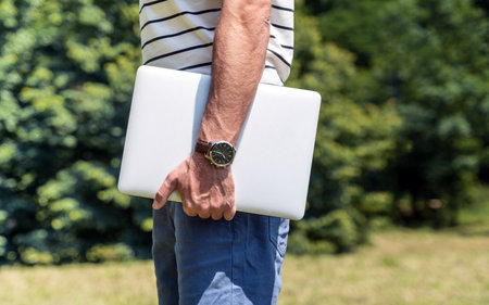 Time saving and portability concept, male person with watch on his wrist holding laptop in hand.の写真素材