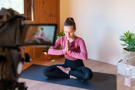 Woman yoga live streamer meditating in front of camera at home.の写真素材