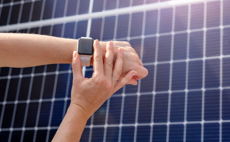 Smartwatch on female hand on background of solar energy panel. remote control of home solar energy station.の写真素材