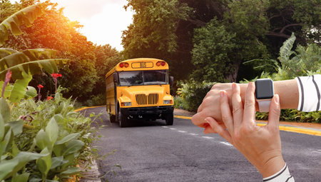Smart watch on hand on background of yellow bus, checking time of departure and arrival of public buses in tropical country.の写真素材