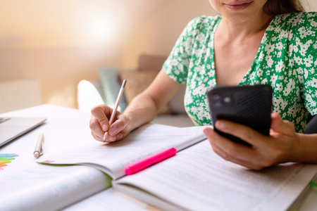 Woman student sitting at the desk doing homework using smart phone.の写真素材