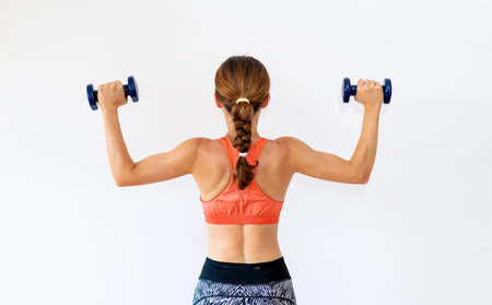 Rear view of sporty female athlete holding dumbbells in her hands.の写真素材