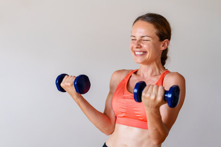 Young female athlete has fun while doing gym exercise with dumbbells.の写真素材