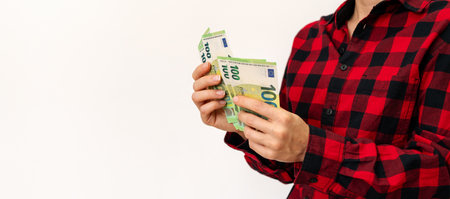 Female person counts euro notes in her hands in front of plain background. Money transfer. Savings...