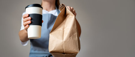 Waitress gives a takeout food order, travel coffee mug and brown paper bag in hands.の写真素材