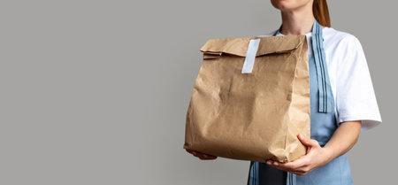 Waitress holds brown package bag for takeout food in her hands. Takeaway food online order.の写真素材