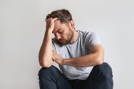 Male mental illness concept. Man sits on the floor and leans his head on his hand.