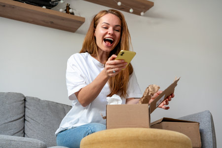 Joyful woman unpacking online purchase and taking picture of goods in cardboard. Home shopping and express delivering.の写真素材